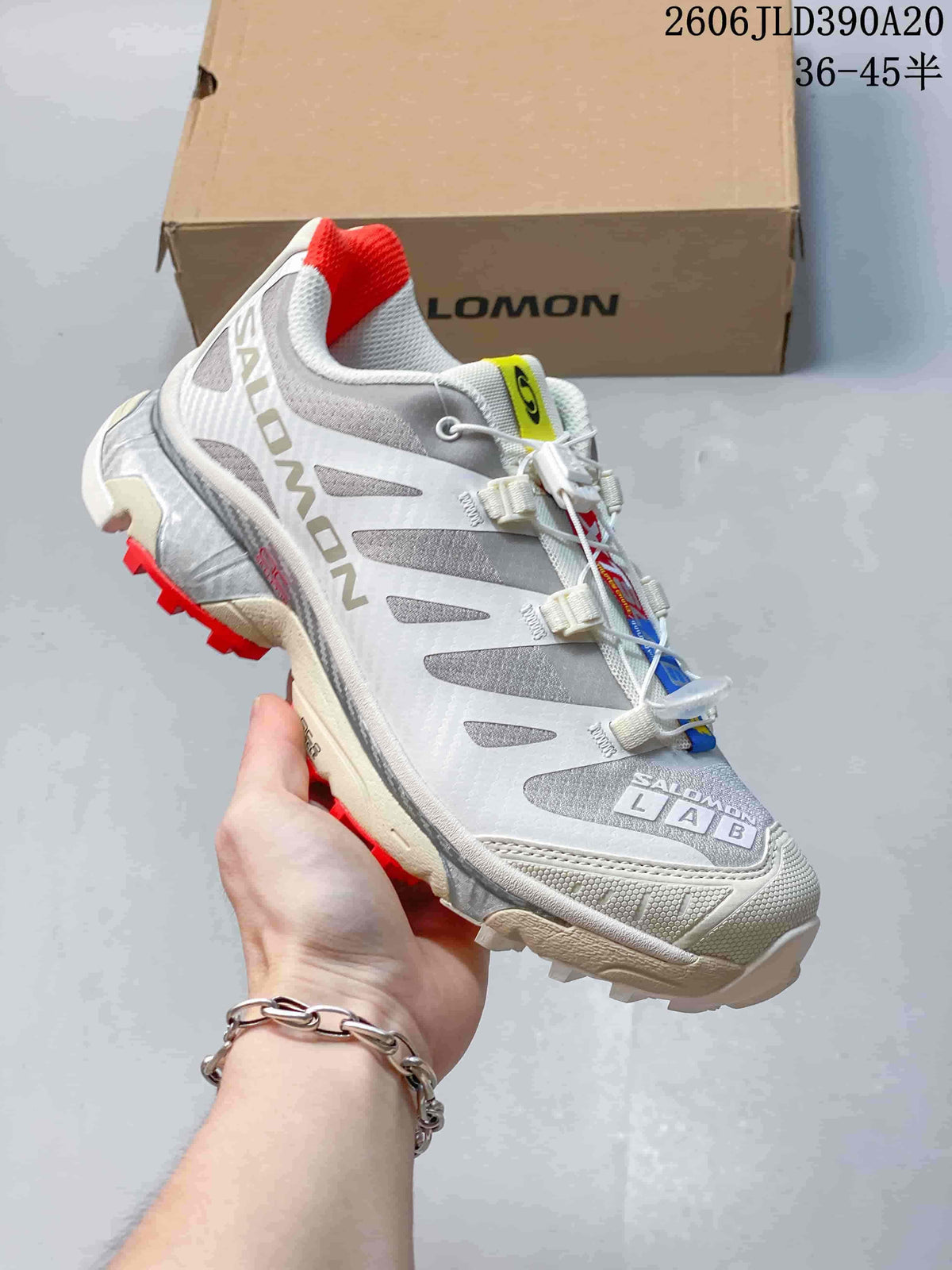 Angled side view of the white and gray Salomon shoe with red accents.