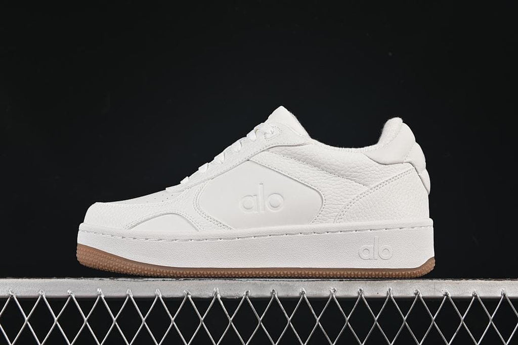 Side view of a white Alo Yoga low-top sneaker with a gum outsole