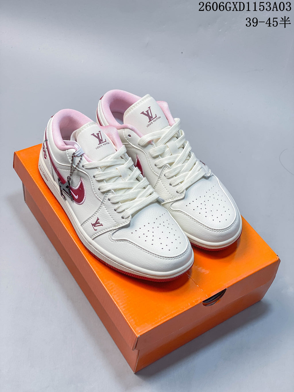 Pair of white and pink low-top sneakers with perforated toes and a metal lace charm, shown on an orange box.