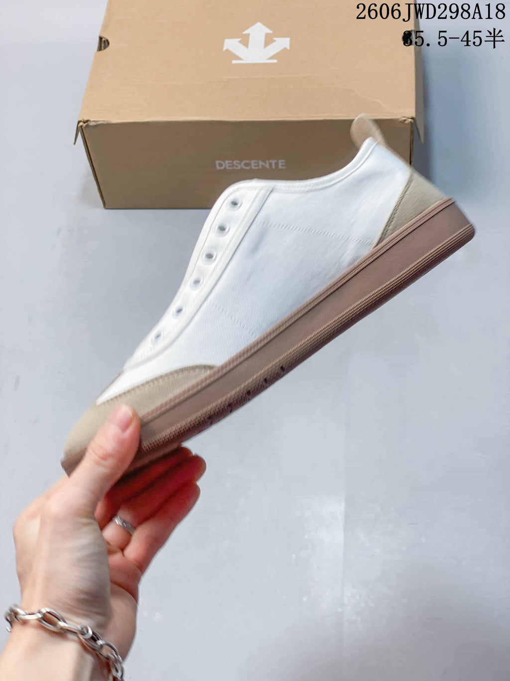Side view of a white and beige Descente sneaker with a brown-toned sole