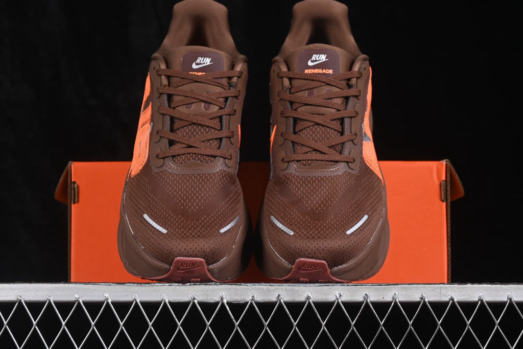 Front view of the pair of brown sneakers positioned over an orange shoebox, with reflective toe accents and orange detailing.