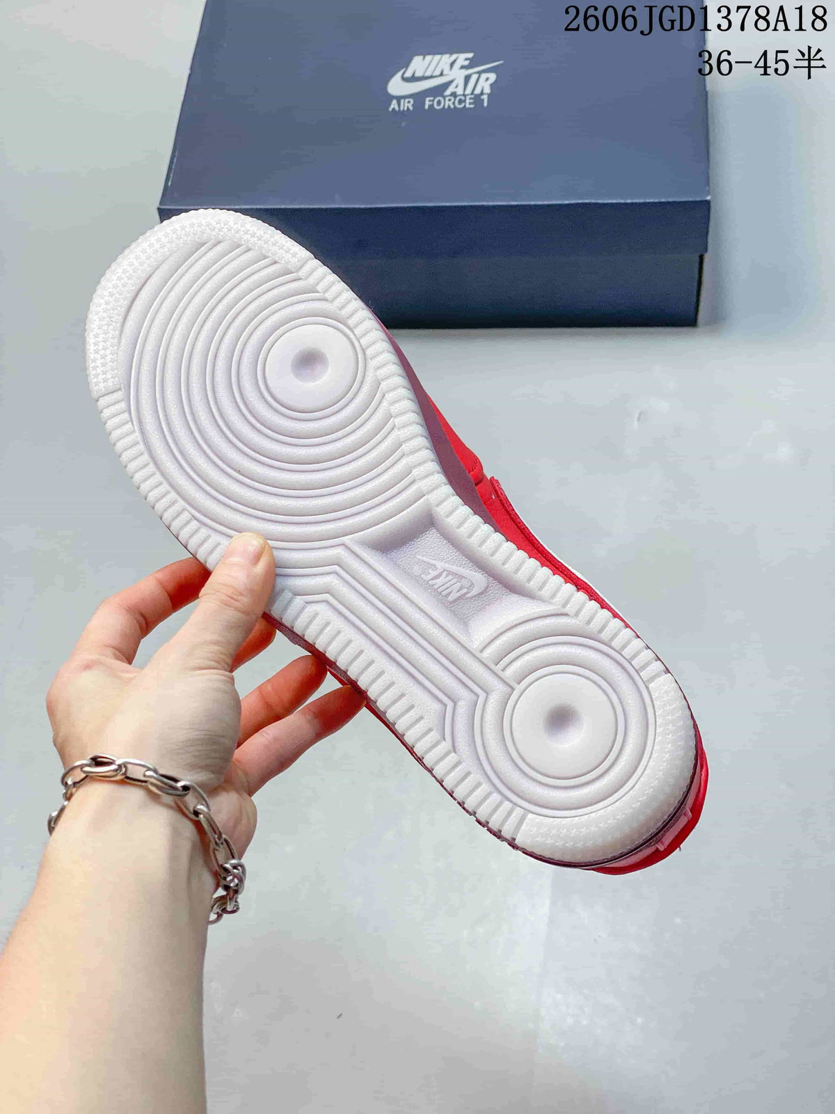 Underside of a red sneaker showing a white circular-pattern outsole and Air Force 1 box