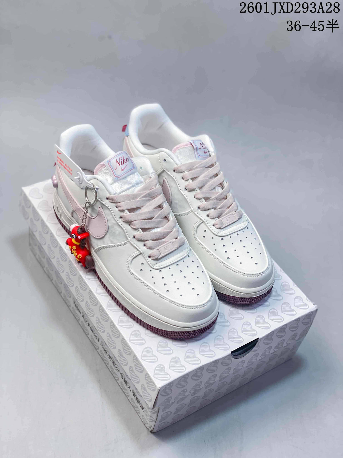 Pair of white and pale pink low-top sneakers with mauve outsoles, bow detail, and character charm on a patterned box.