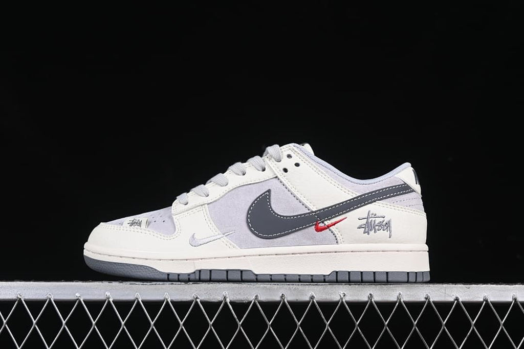 Side view of off-white and grey Nike Dunk Low sneakers with dark grey Swoosh and red accent