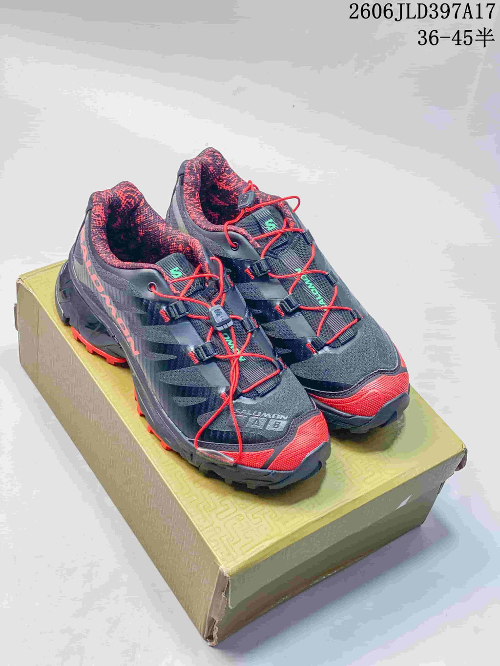 Pair of dark gray and black Salomon XT-4 OG shoes with red accents, shown on a shoe box