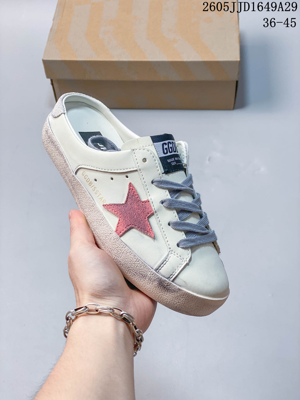 Angled side view of a white backless sneaker with a pink star and gray laces