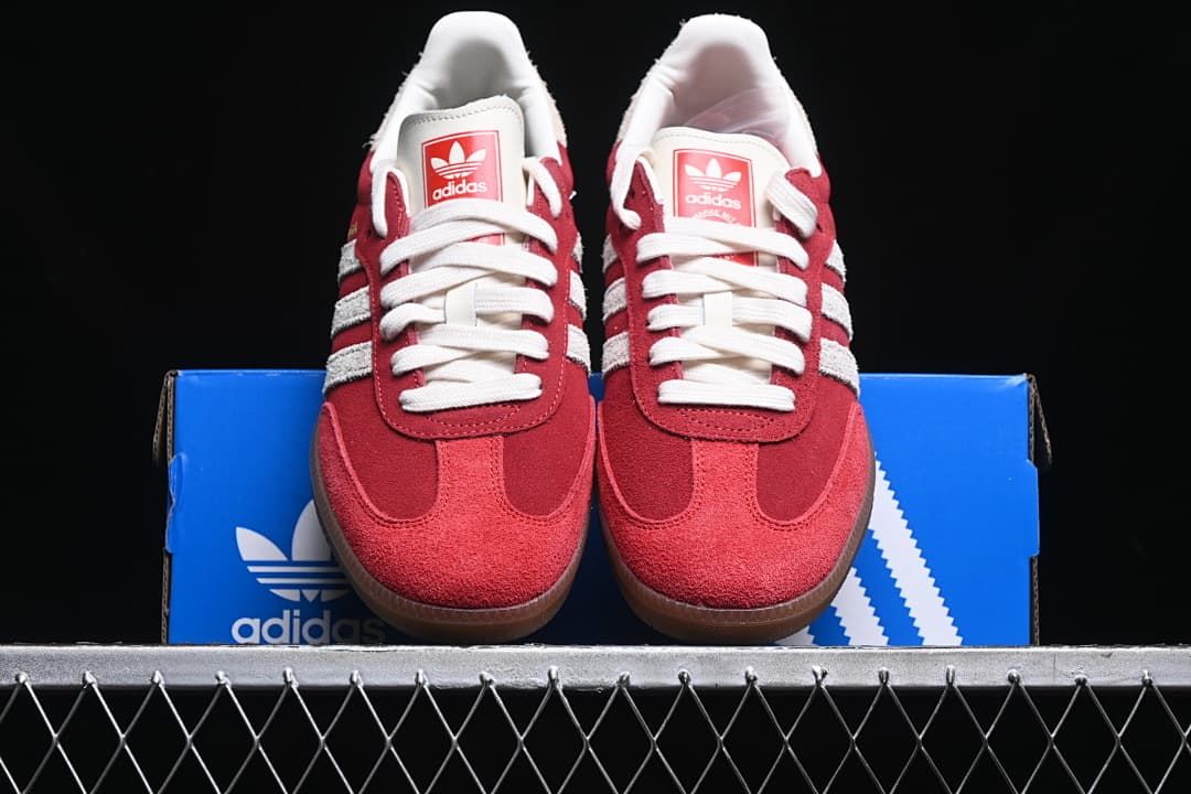 Front view of the red sneakers displayed on a blue adidas shoe box.