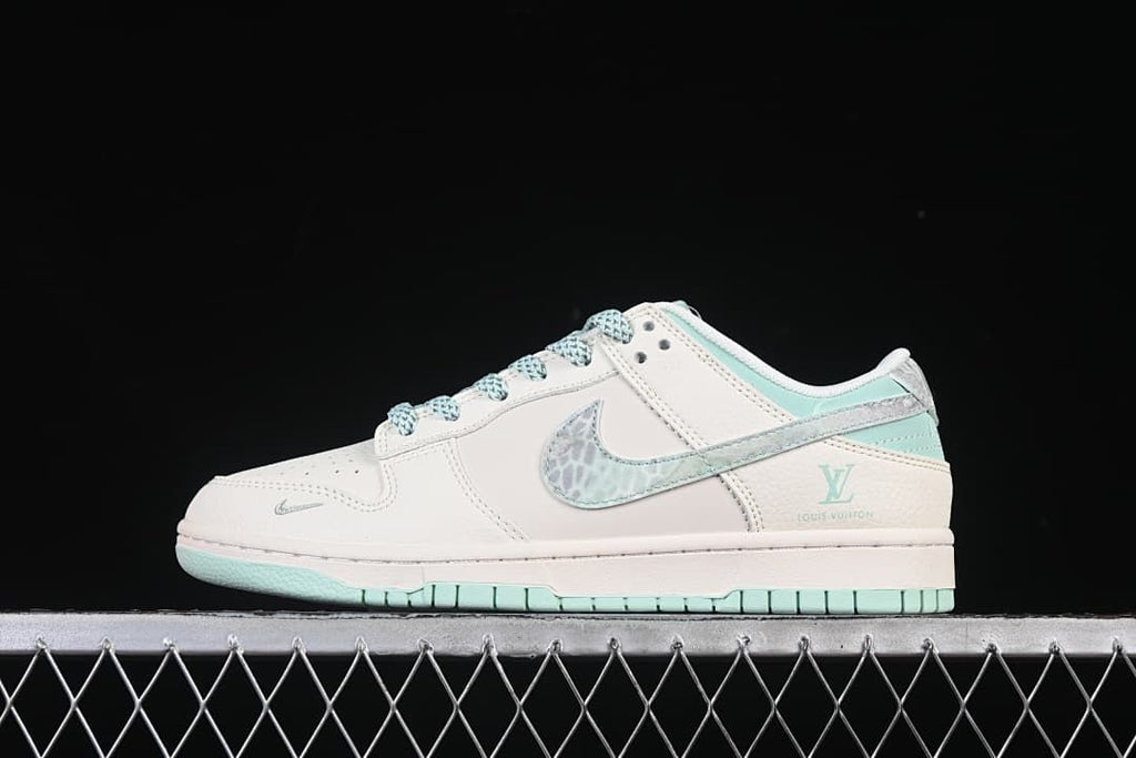 Side view of an off-white and mint-green Nike SB Dunk Low sneaker with patterned Swoosh and heel accents.