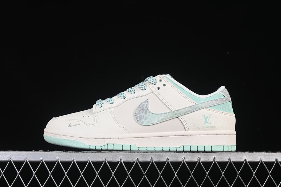 Side view of an off-white and mint-green Nike SB Dunk Low sneaker with patterned Swoosh and heel accents.