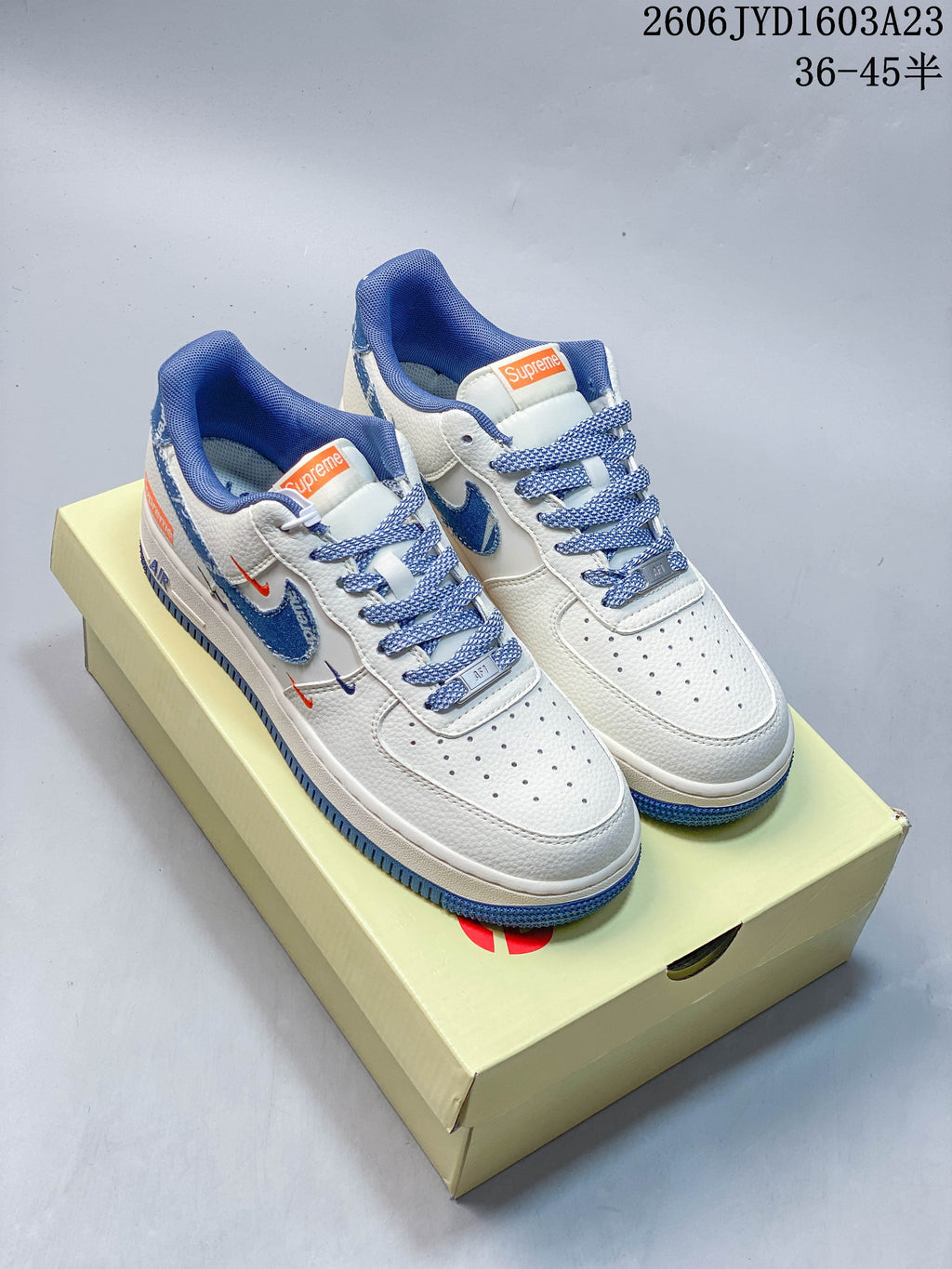 Pair of white low-top sneakers with blue accents and patterned laces, shown on a shoebox