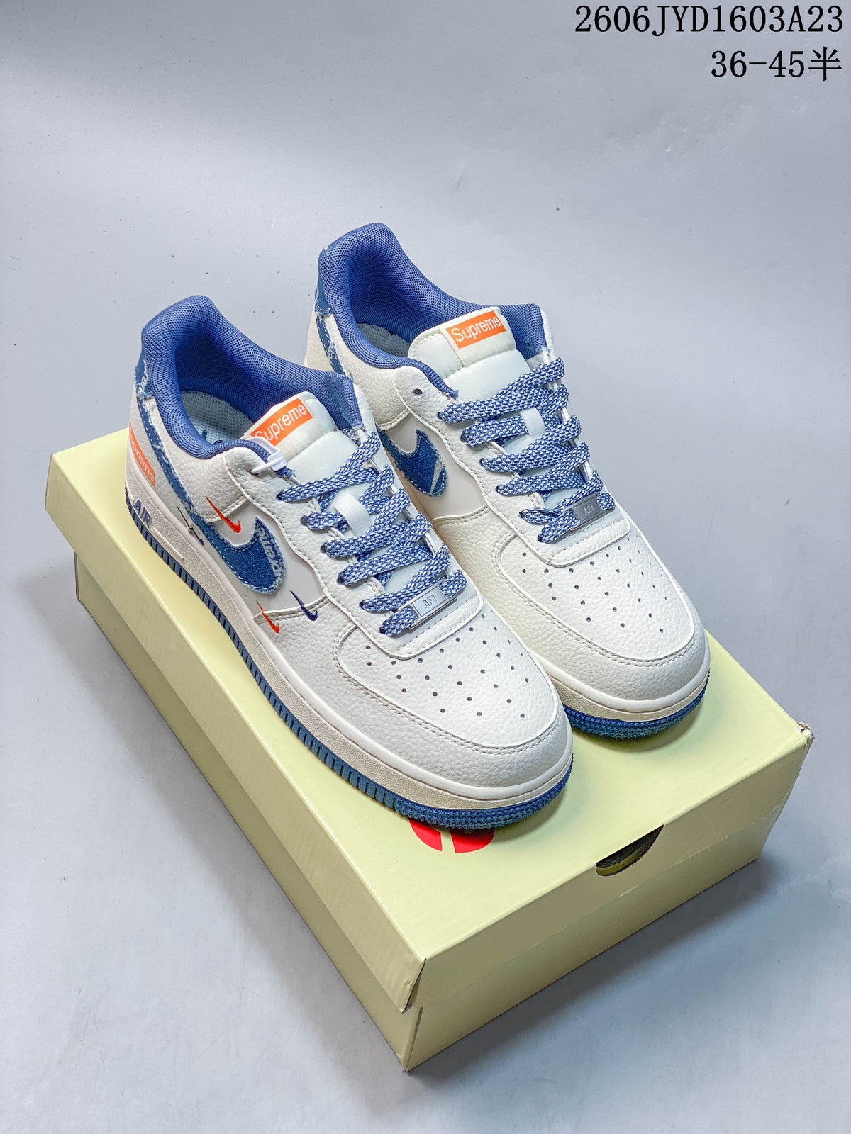 Pair of white low-top sneakers with blue accents and patterned laces, shown on a shoebox