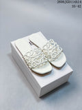 Pair of white Loewe-style flat slide sandals with sculptural interlaced straps, shown on a box