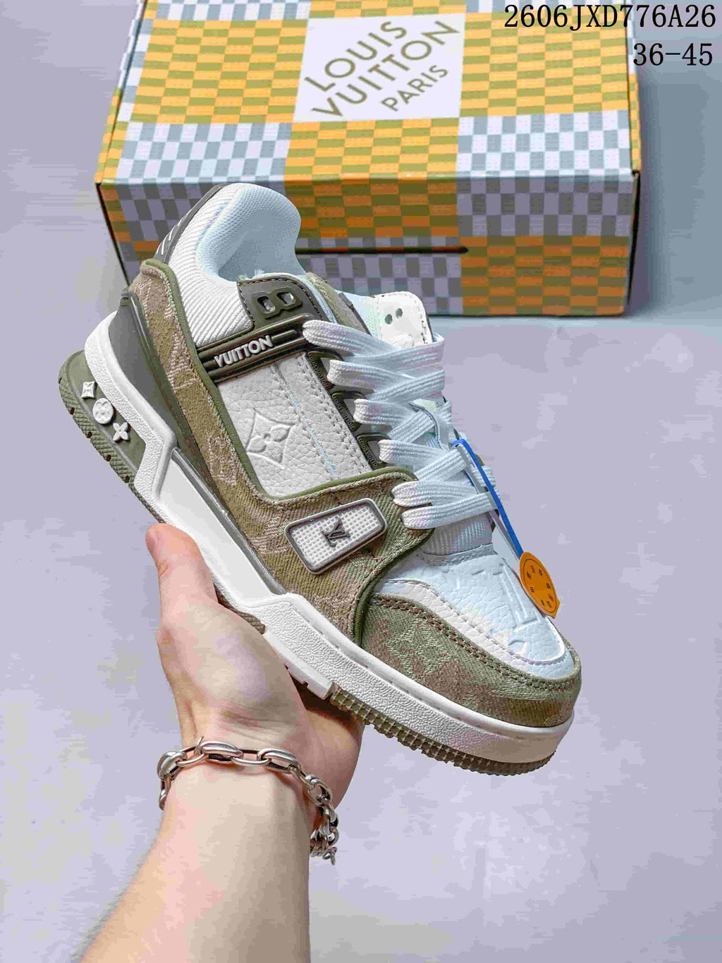 Close-up of a white and muted olive Louis Vuitton Trainer Low sneaker with a patterned box behind it