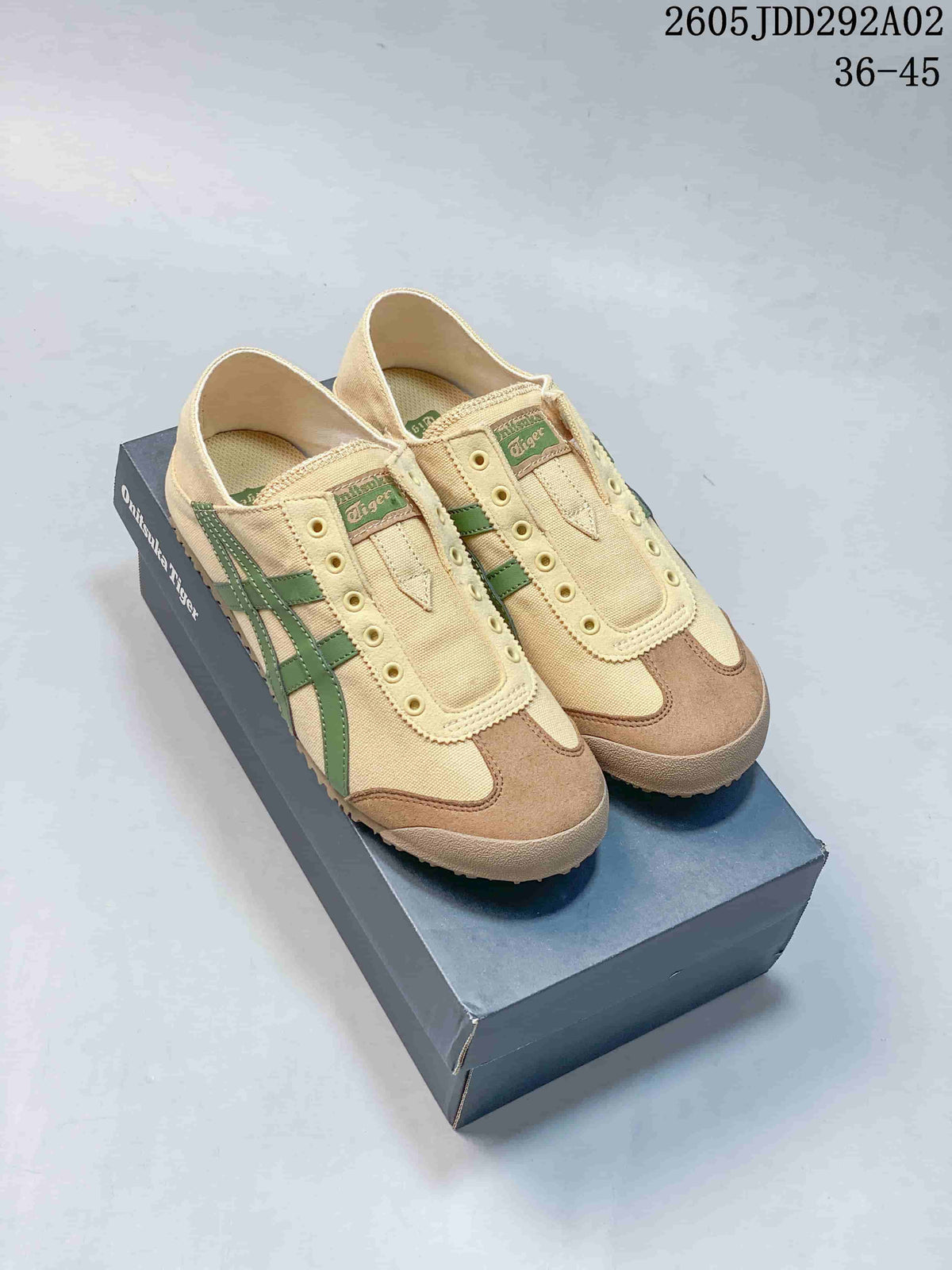 Pair of beige Onitsuka Tiger slip-on sneakers with green stripes and brown-toned toe overlays, shown on a shoe box.