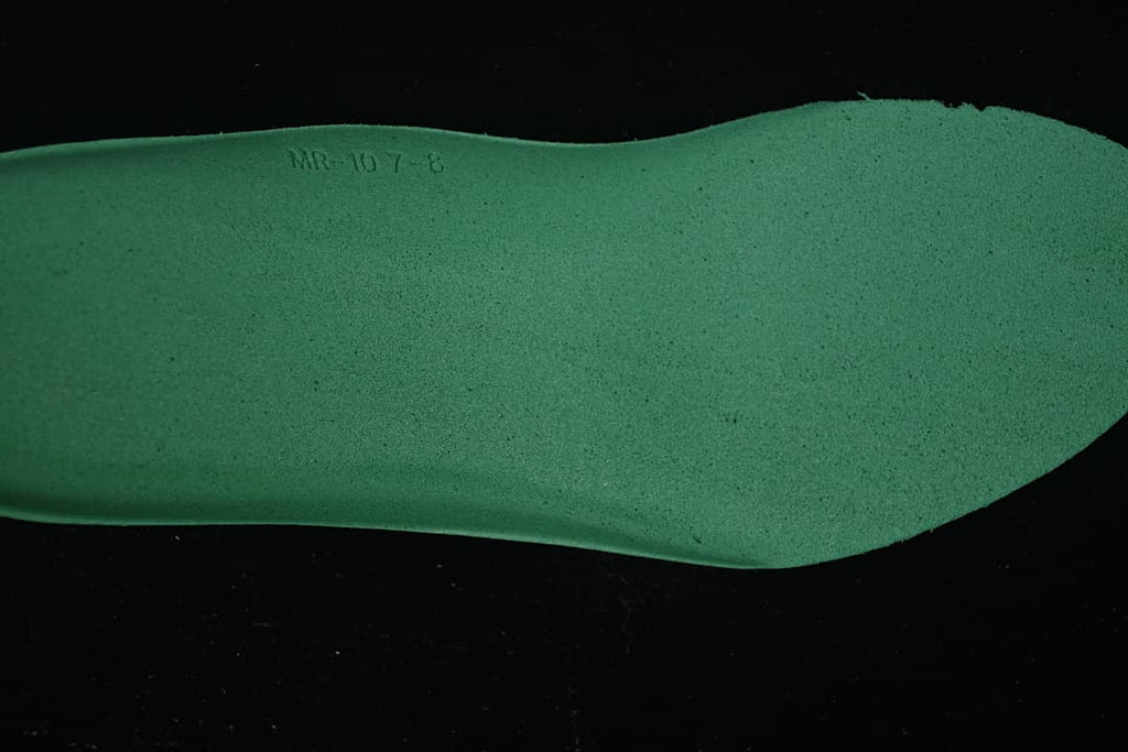 Close-up of a green shoe component with a small embossed marking.