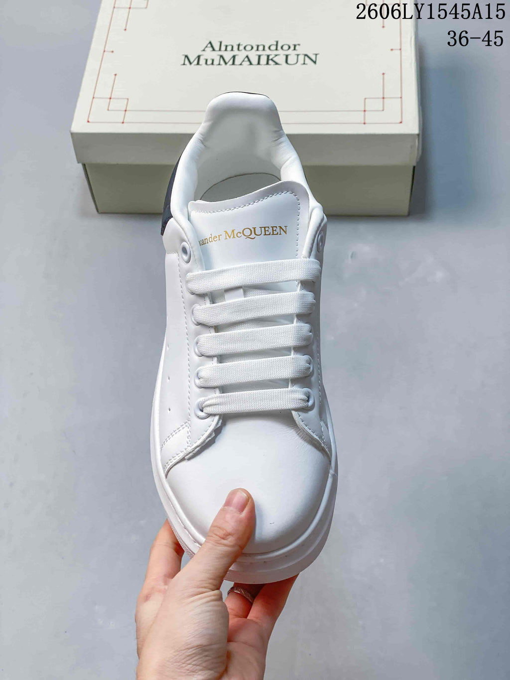 Front view of a white lace-up sneaker with gold-tone tongue lettering.