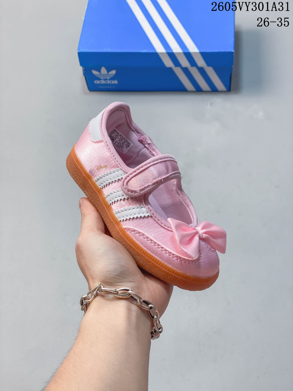 Angled side view of a pink kids’ shoe with white stripes, a bow, and a gum-colored sole.