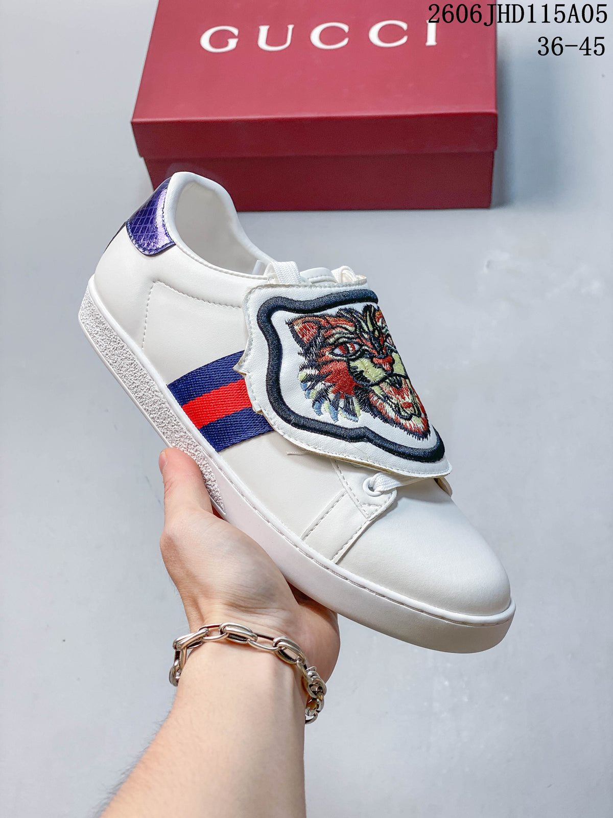White low-top sneaker with an embroidered feline-face tongue flap, red-and-blue side stripe, and purple heel accent.