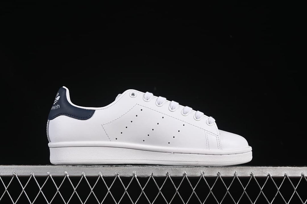 Side profile of the white sneaker with perforated panels and navy heel tab.