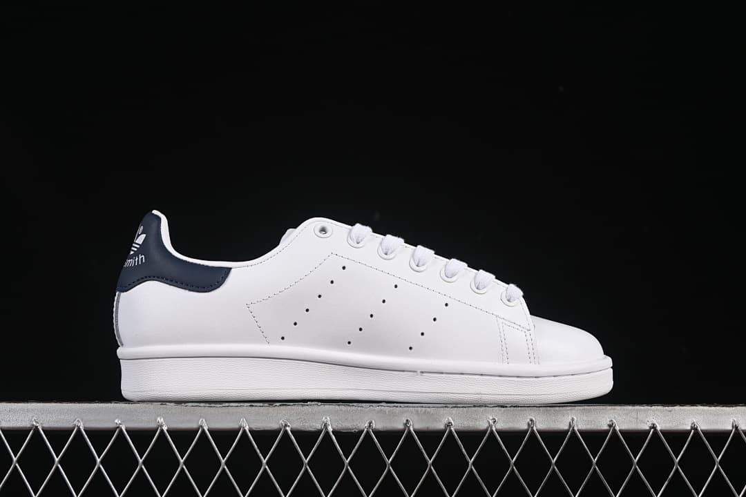 Side profile of the white sneaker with perforated panels and navy heel tab.