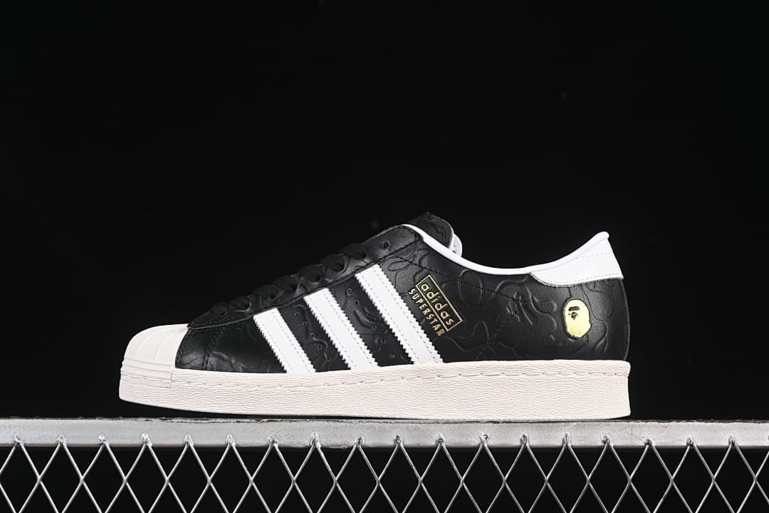 Side view of a black and white adidas Superstar sneaker with embossed upper and gold-tone accents