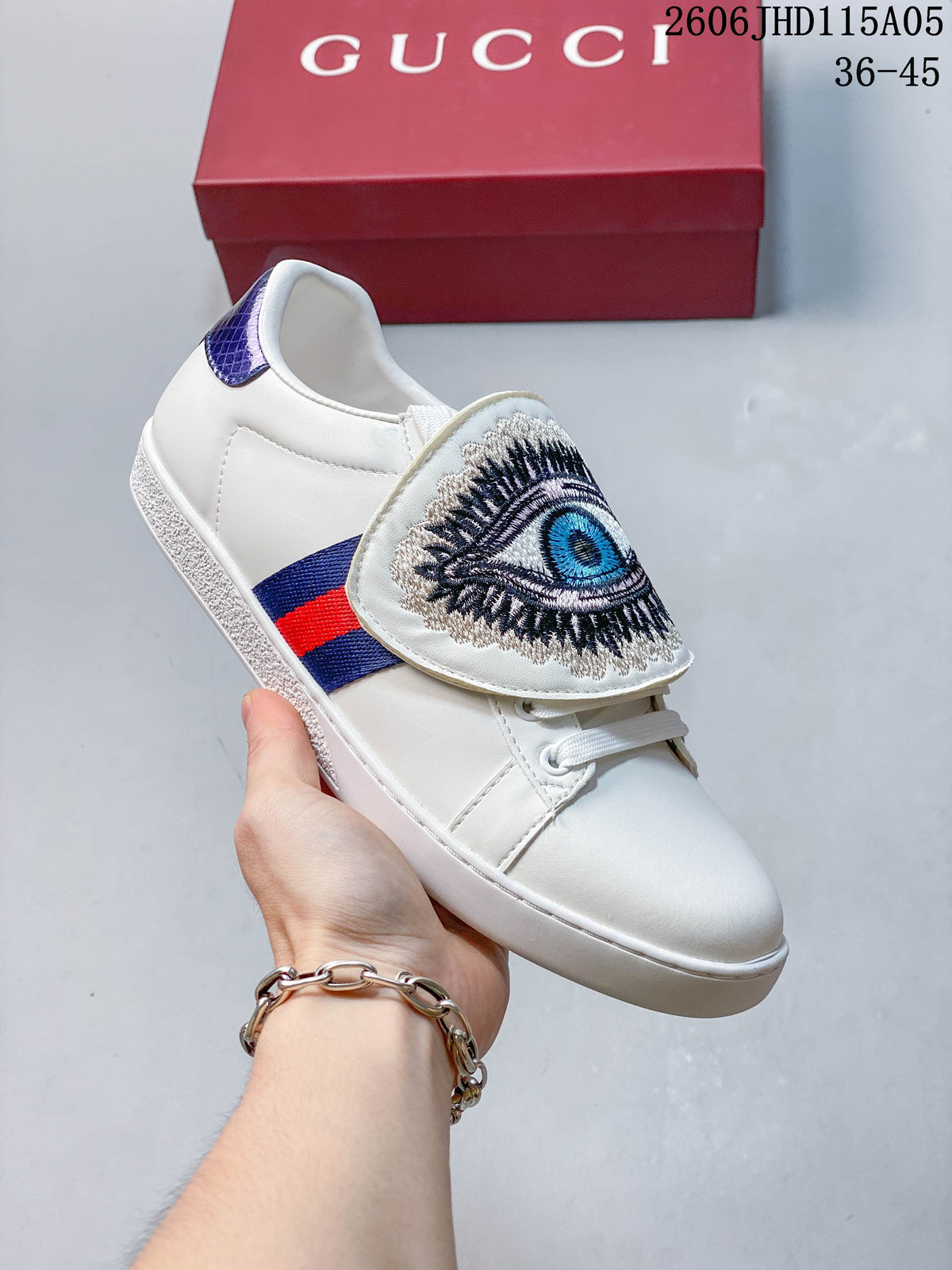White low-top sneaker with an embroidered eye motif on the tongue flap.