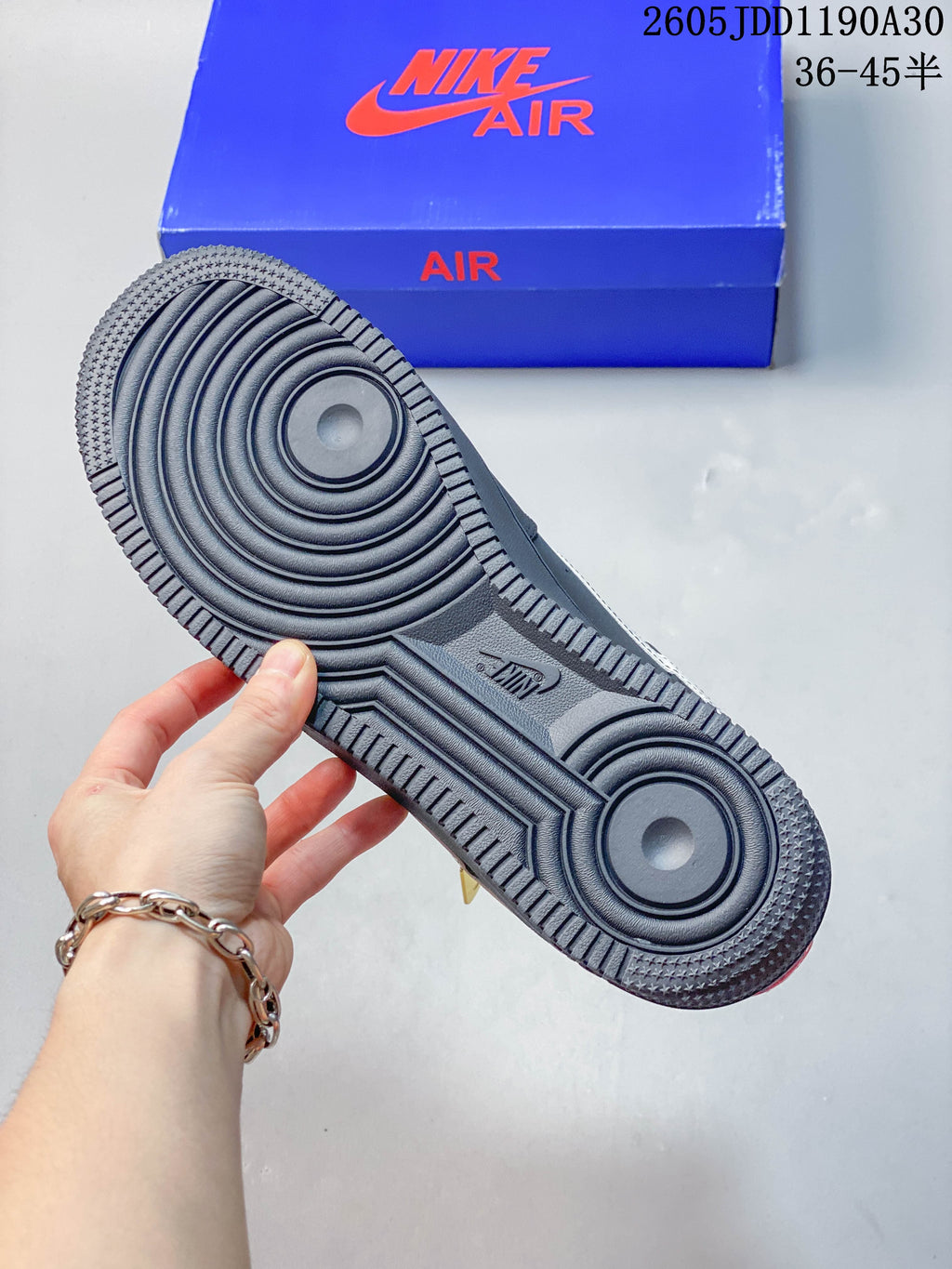 View of the dark gray sneaker outsole with circular tread and a blue box in the background.