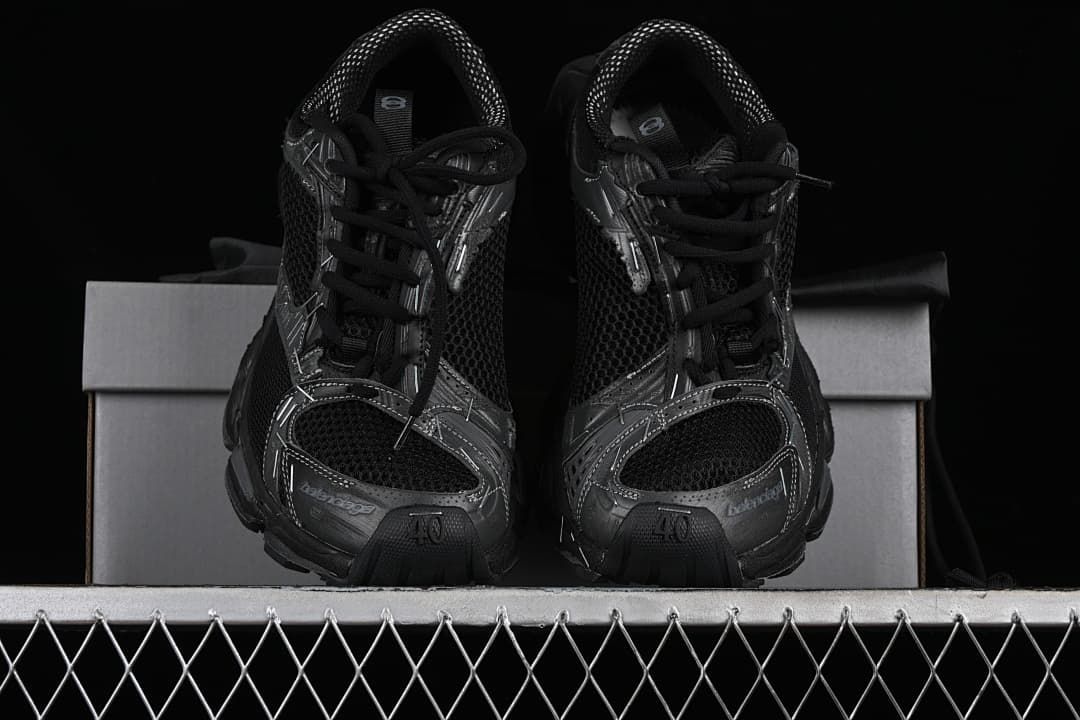 Pair of black sneakers viewed from the front, displayed on a box.