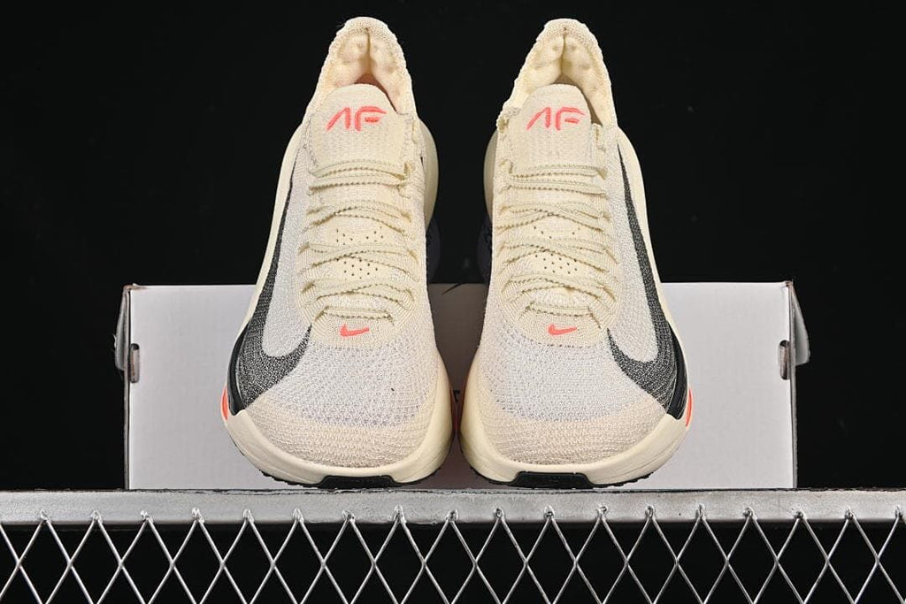Front view of the pair of cream shoes with black Swooshes and coral details
