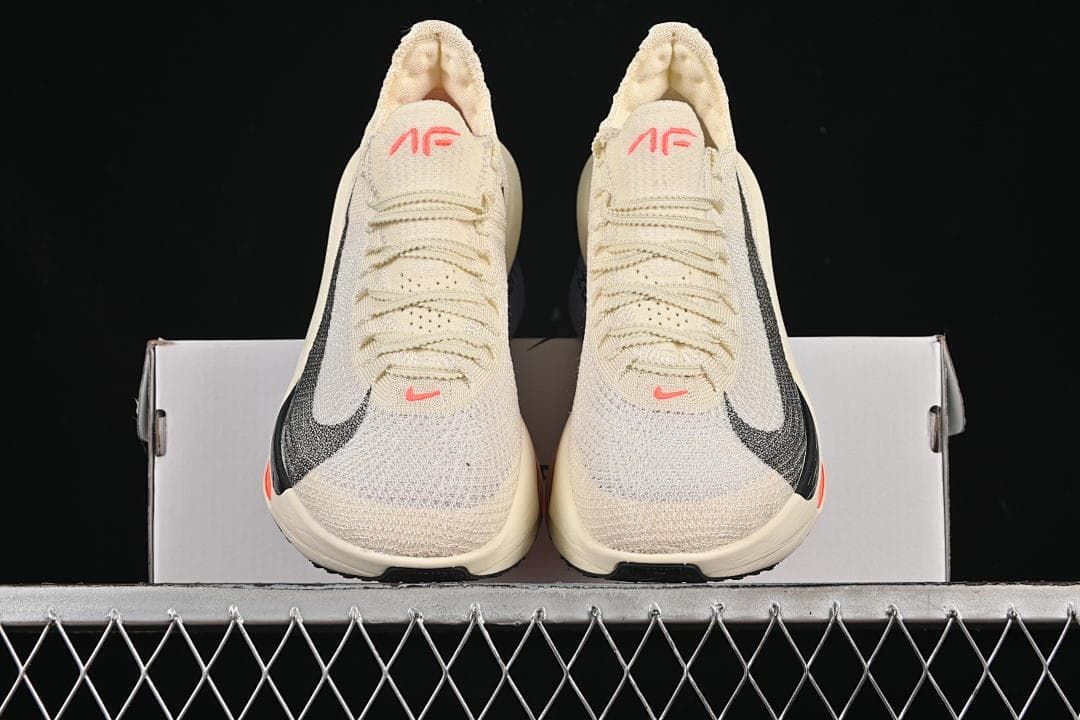 Front view of the pair of cream shoes with black Swooshes and coral details
