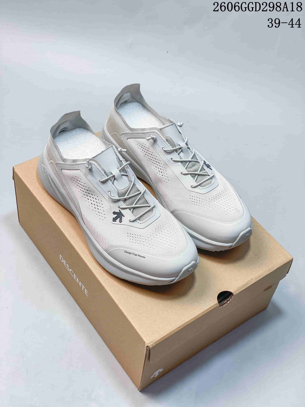 Pair of light gray DESCENTE low-top sneakers with perforated uppers and lace-style closures, displayed on a shoebox.