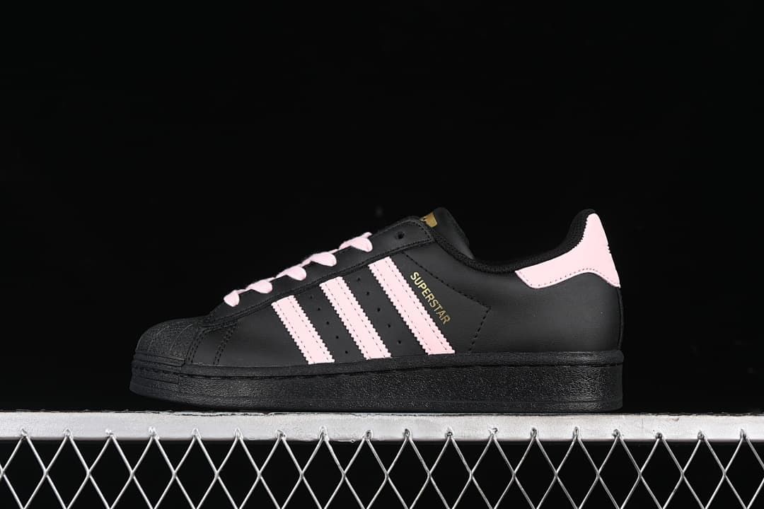 Side view of a black adidas Superstar sneaker with pink accents