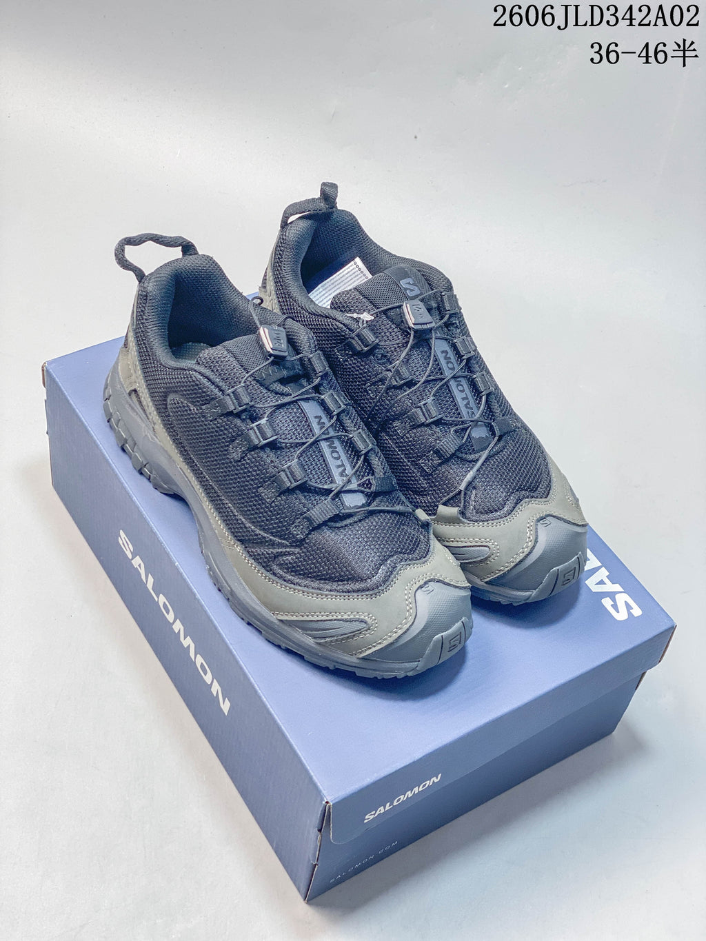 Gray Salomon trail shoes shown on a branded box; image overlay includes the product code and a size range.