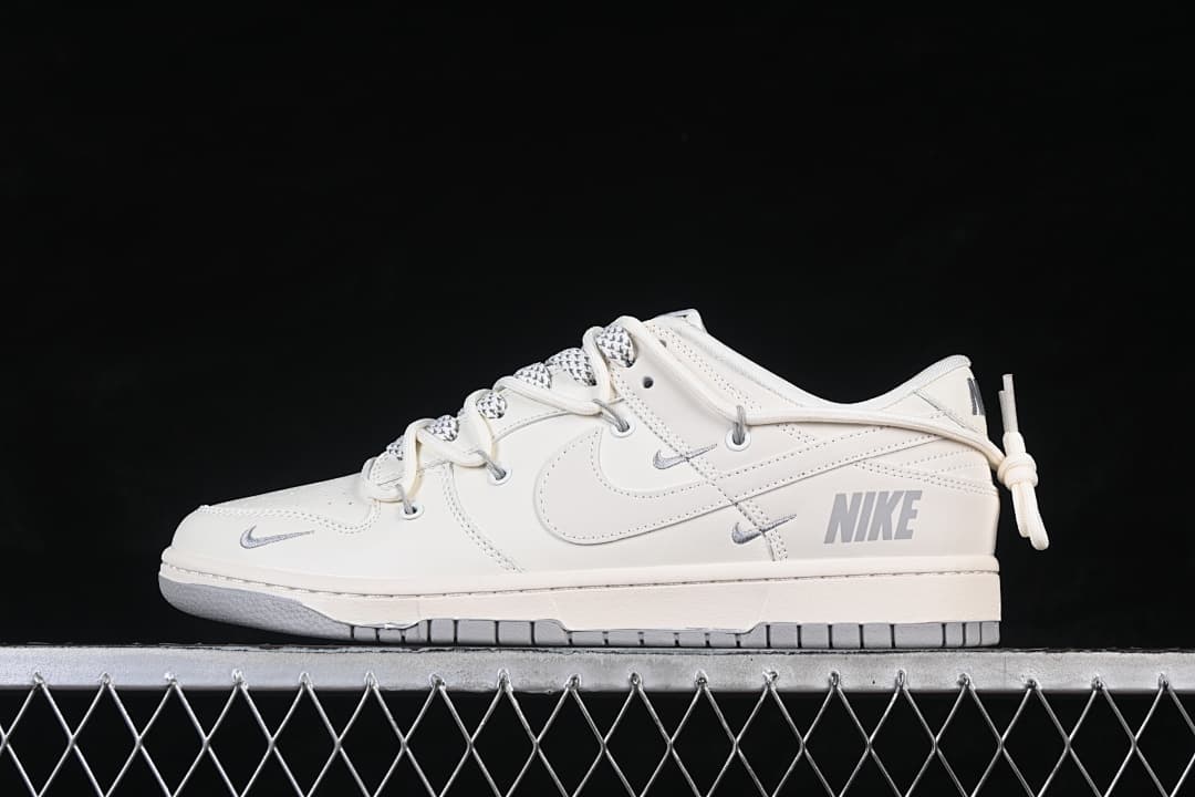Side view of a cream Nike SB Dunk Low sneaker with gray accents and decorative heel cord