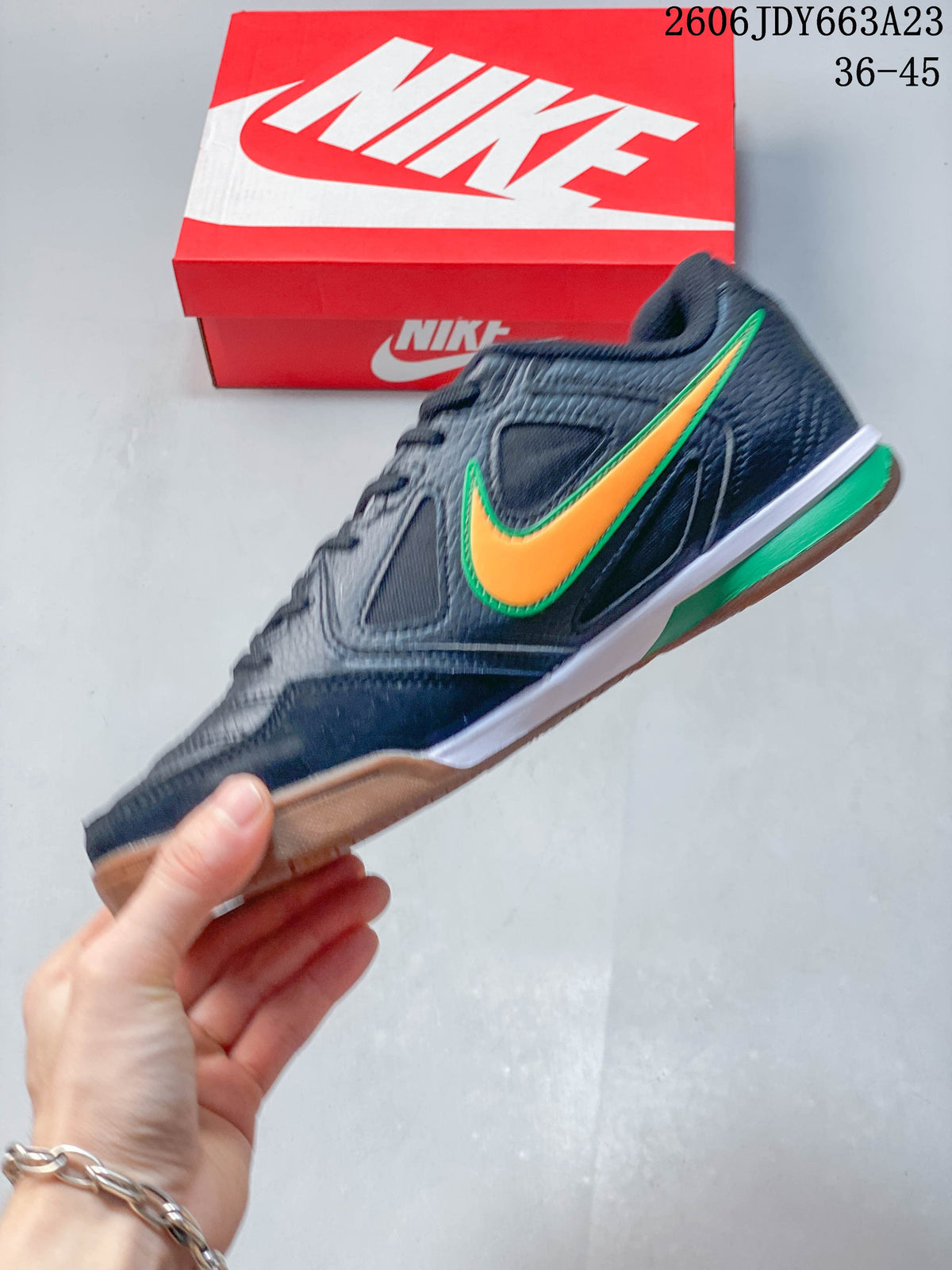 Side view of a dark low-top sneaker with orange and green accents and a gum-colored outsole
