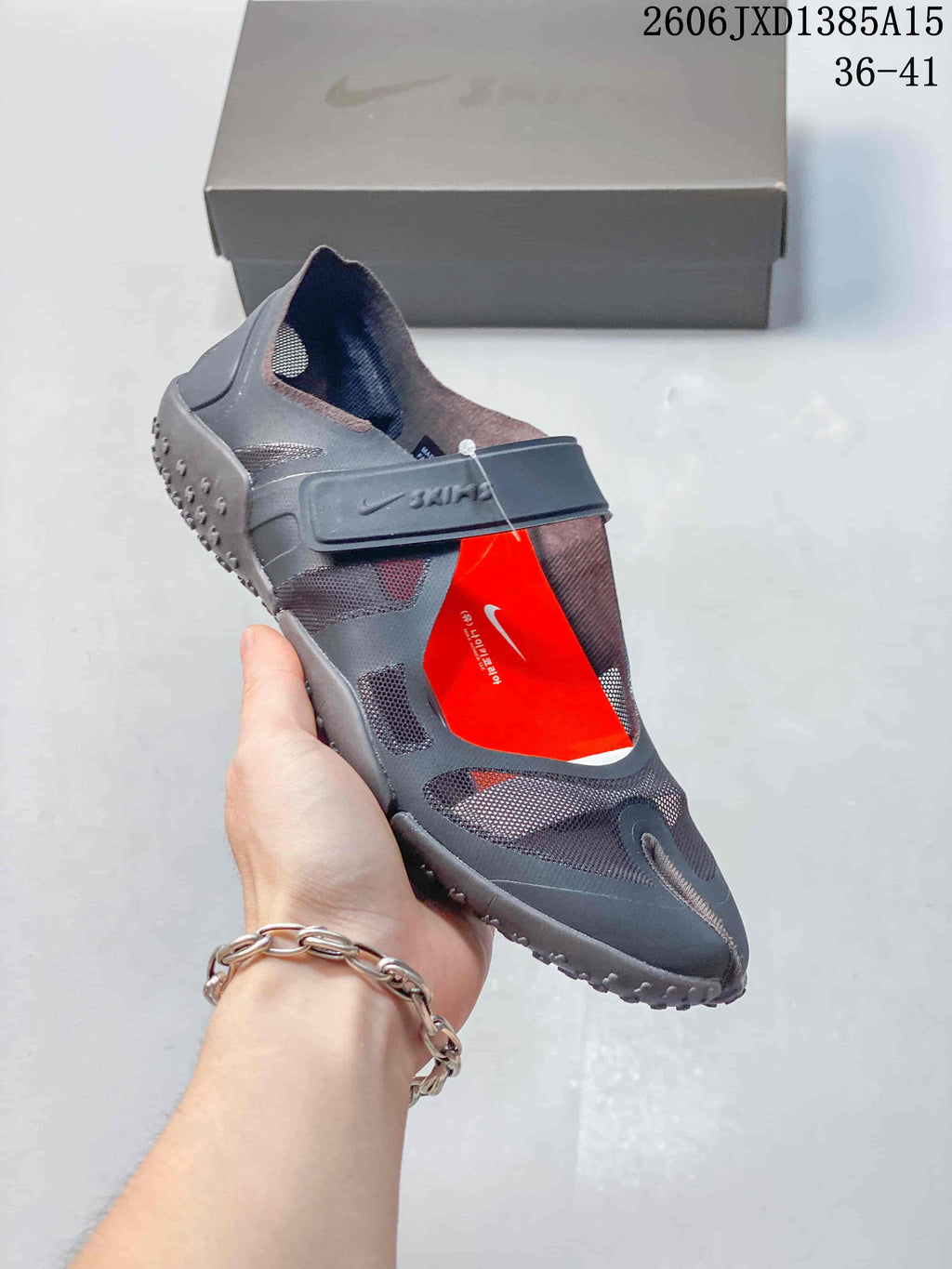 Angled view of a dark gray Nike Air Rift shoe with mesh panels, a wide strap, and red accents.