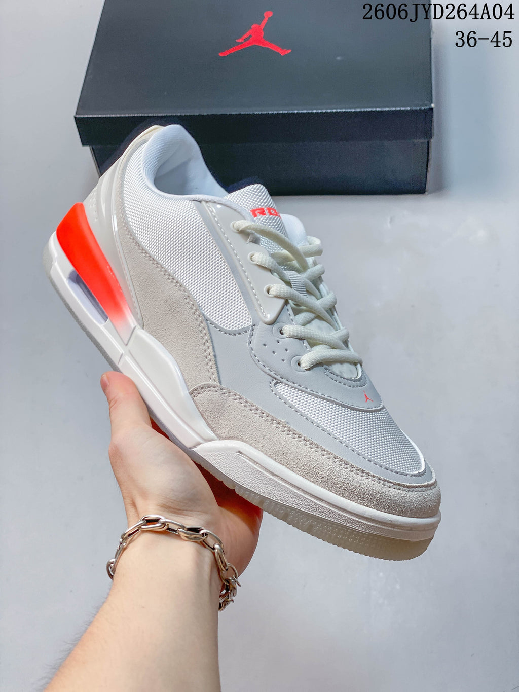 Angled side view of a sail and gray Jordan low-top sneaker with red-orange heel accents