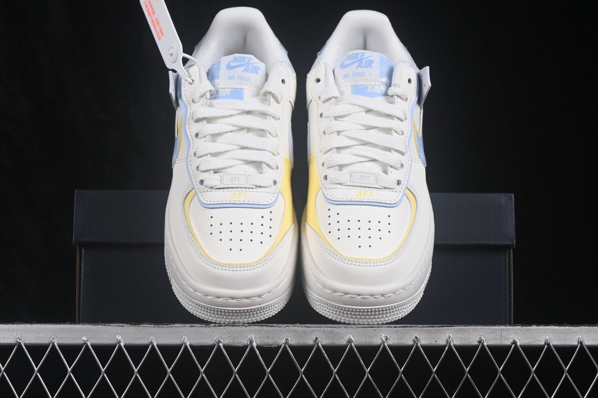 Pair of white Nike Air Force 1 Shadow sneakers with light blue and yellow accents shown from the front.