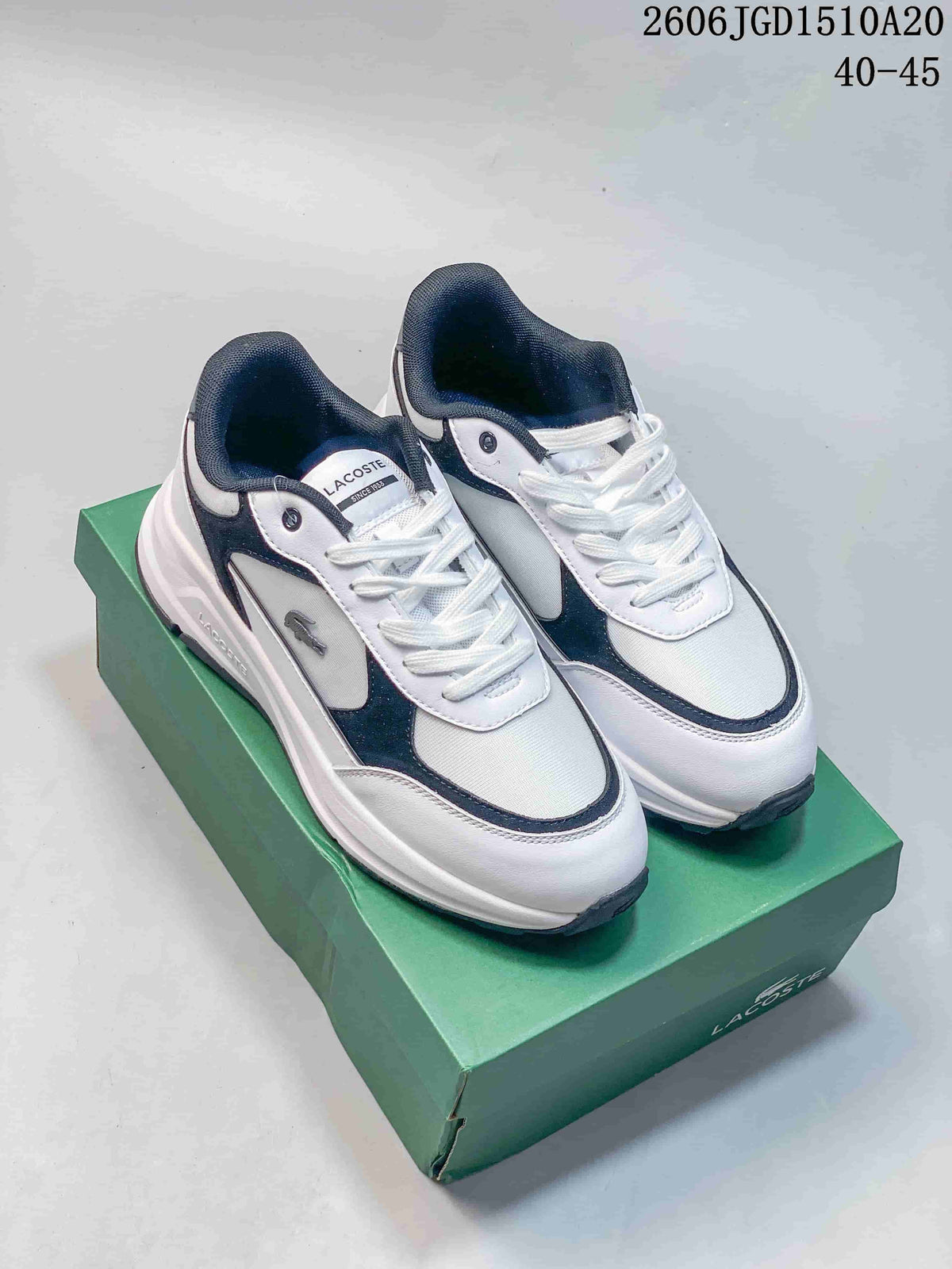 Pair of white Lacoste low-top sneakers with navy and gray accents, shown on a green shoe box