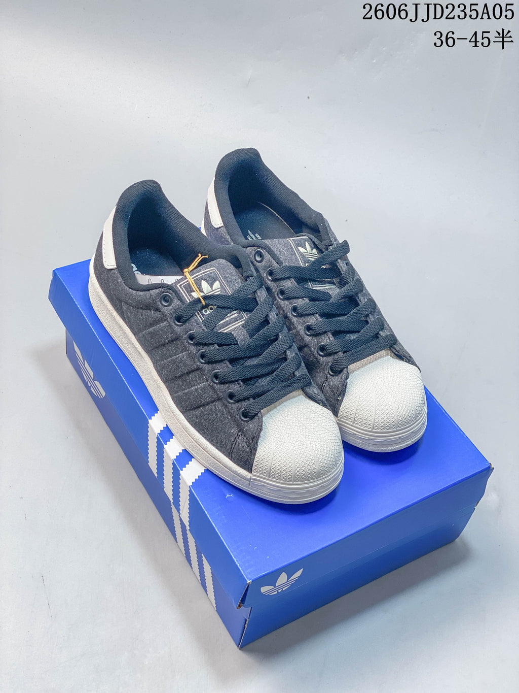Pair of charcoal gray Adidas Originals Superstar low-top sneakers with white shell toes on a blue shoebox