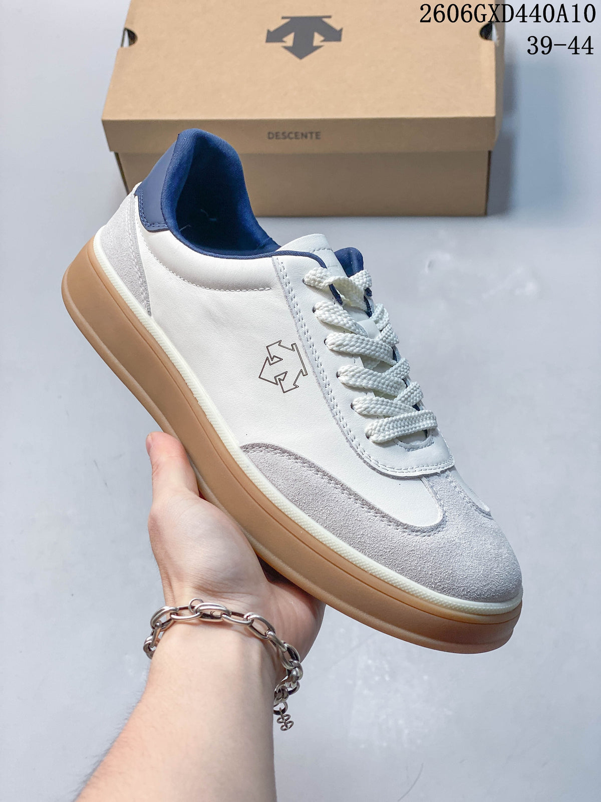 Angled side view of the white and gray DESCENTE sneaker with navy accents and a gum-colored sole.