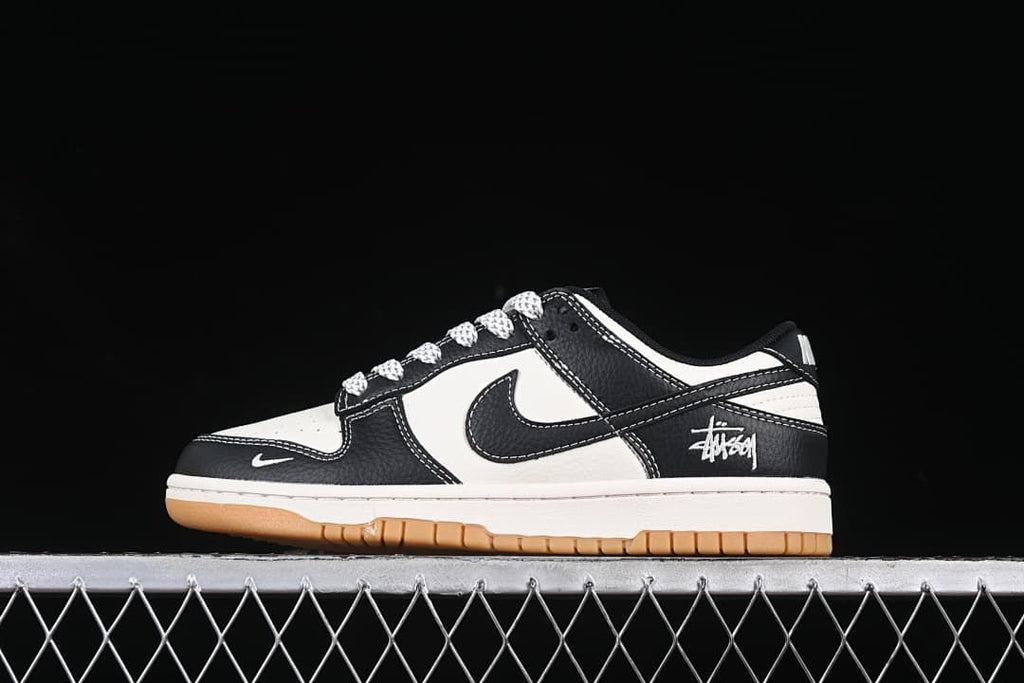 Side view of black and white low-top sneakers with patterned laces, heel script, and gum-colored outsole