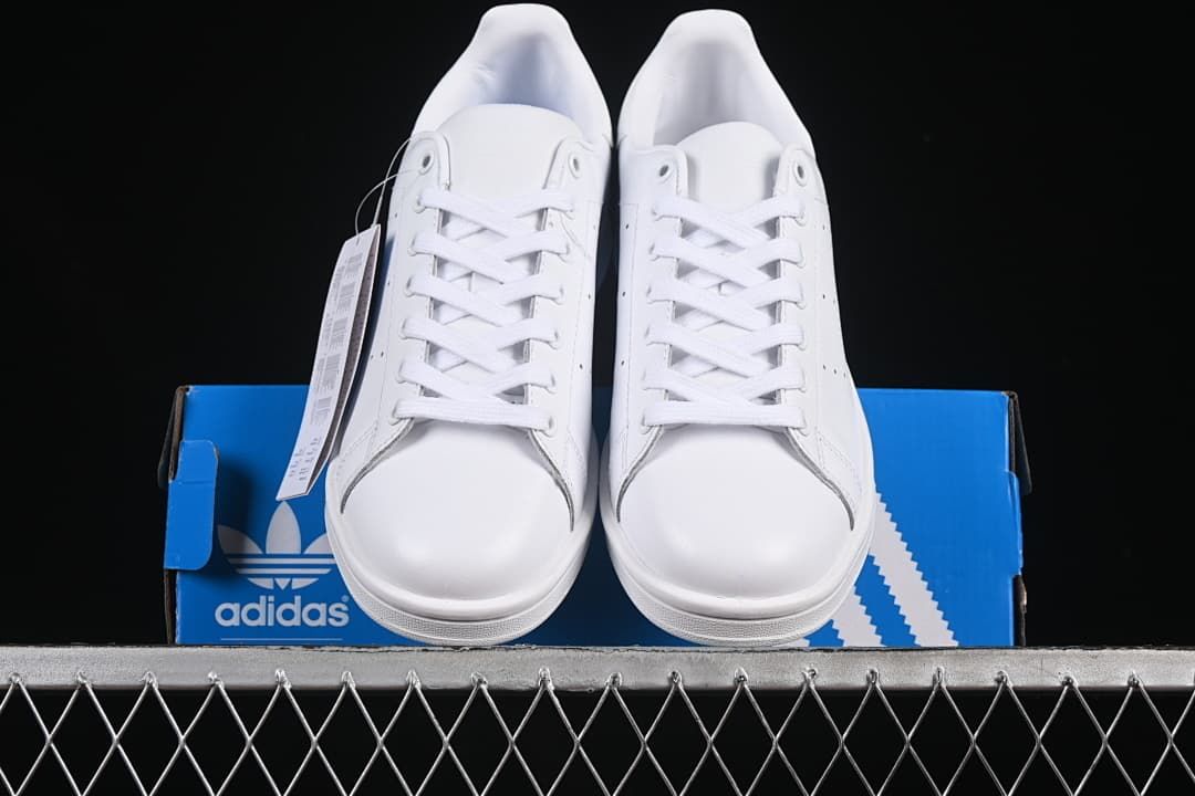 Front view of the pair of white lace-up sneakers on a blue box