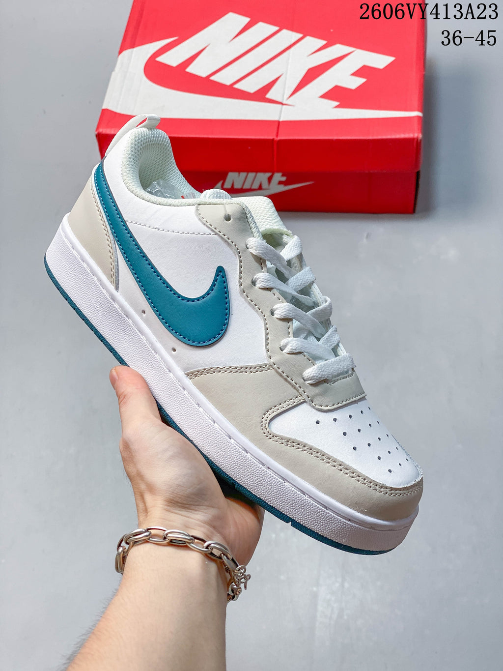 White low-top sneaker with teal Swoosh and beige overlays, held in front of a Nike shoe box