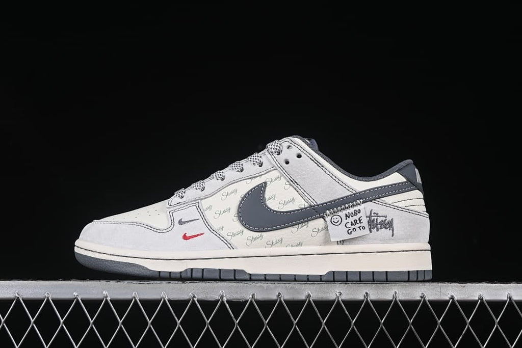 Side profile of a light grey Nike SB Dunk Low sneaker with a dark grey Swoosh and script-patterned panels