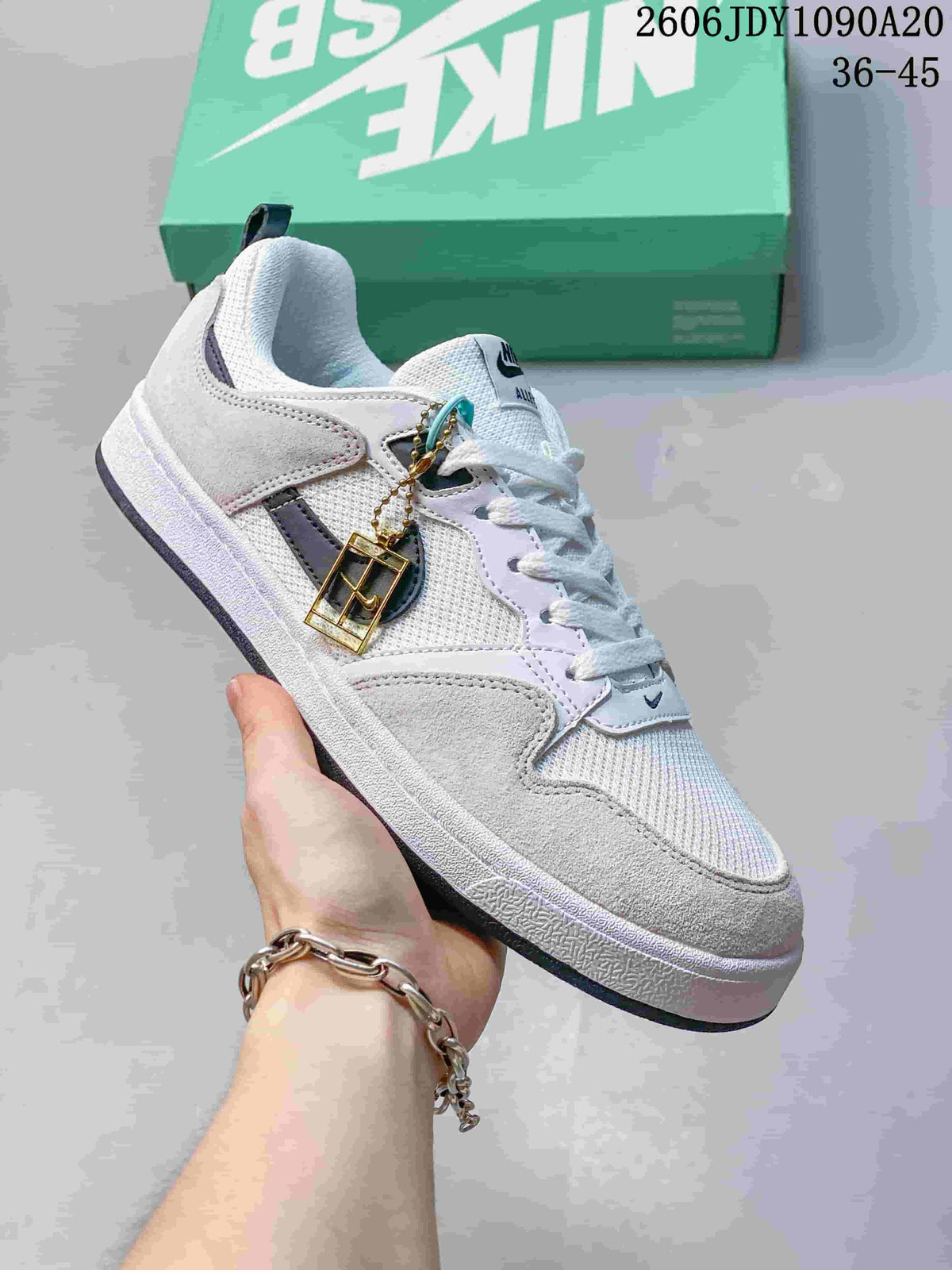 Angled side view of a white and light grey Nike SB Alleyoop shoe with lace charm
