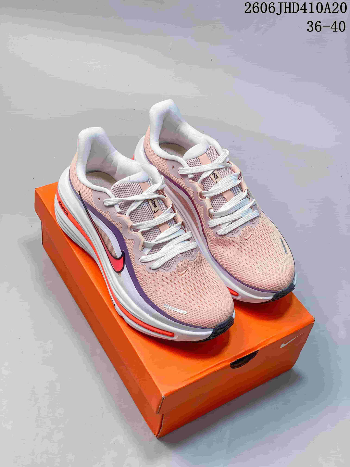 Pale pink Nike Air Zoom Winflo 12 running shoes with purple and orange accents, displayed on an orange shoebox.