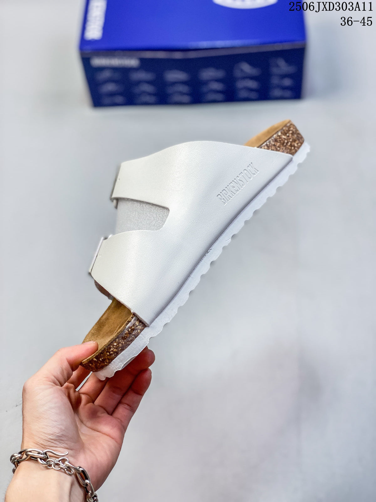 Side view of a white two-strap sandal with a brown footbed and cork-look midsole.