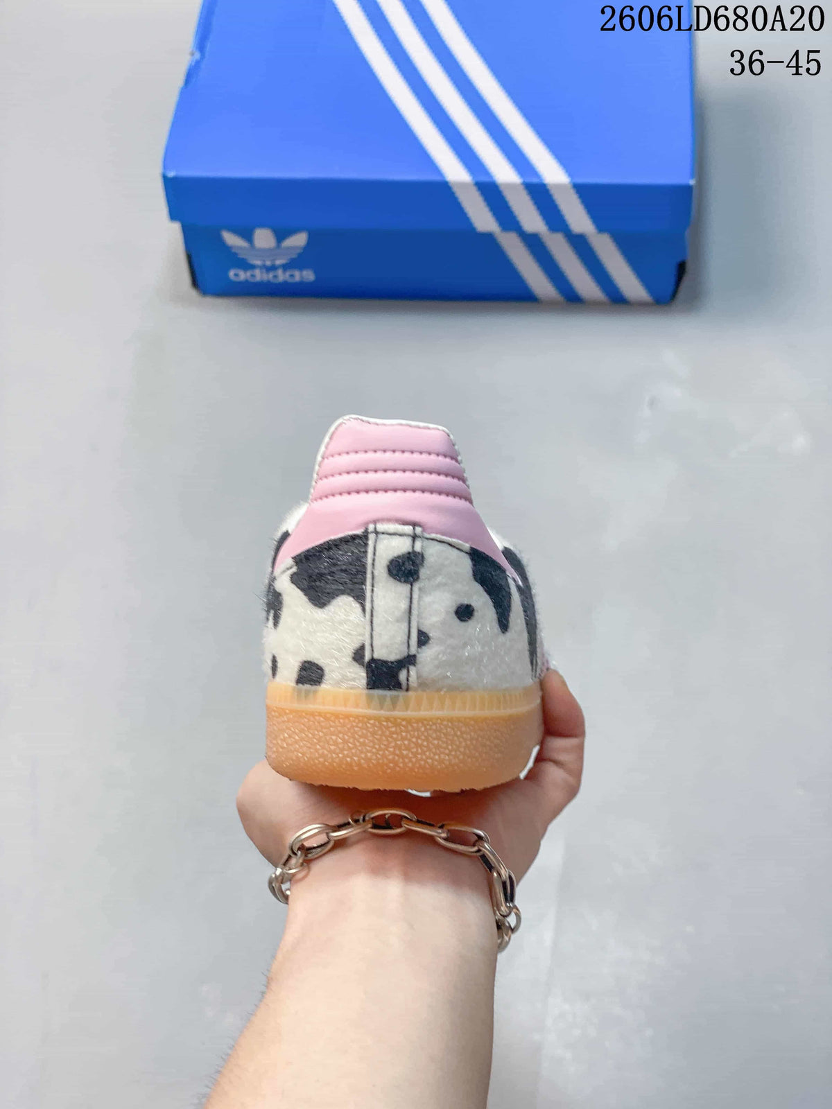 Rear view of a cow-print Adidas Samba OG sneaker with a pink heel accent and gum-colored outsole