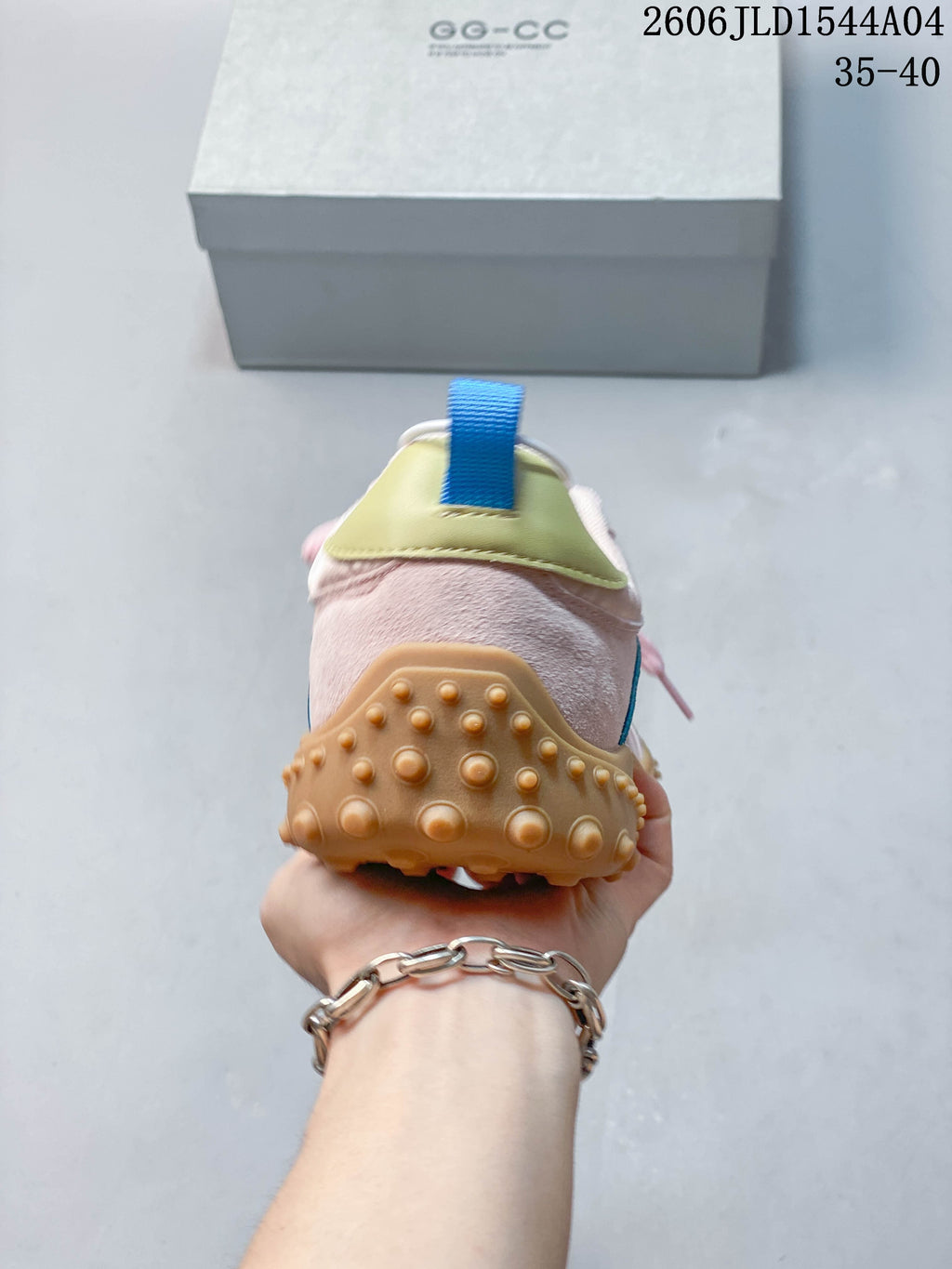 Rear view showing the pale pink heel, light yellow heel tab, blue pull loop, and tan outsole.